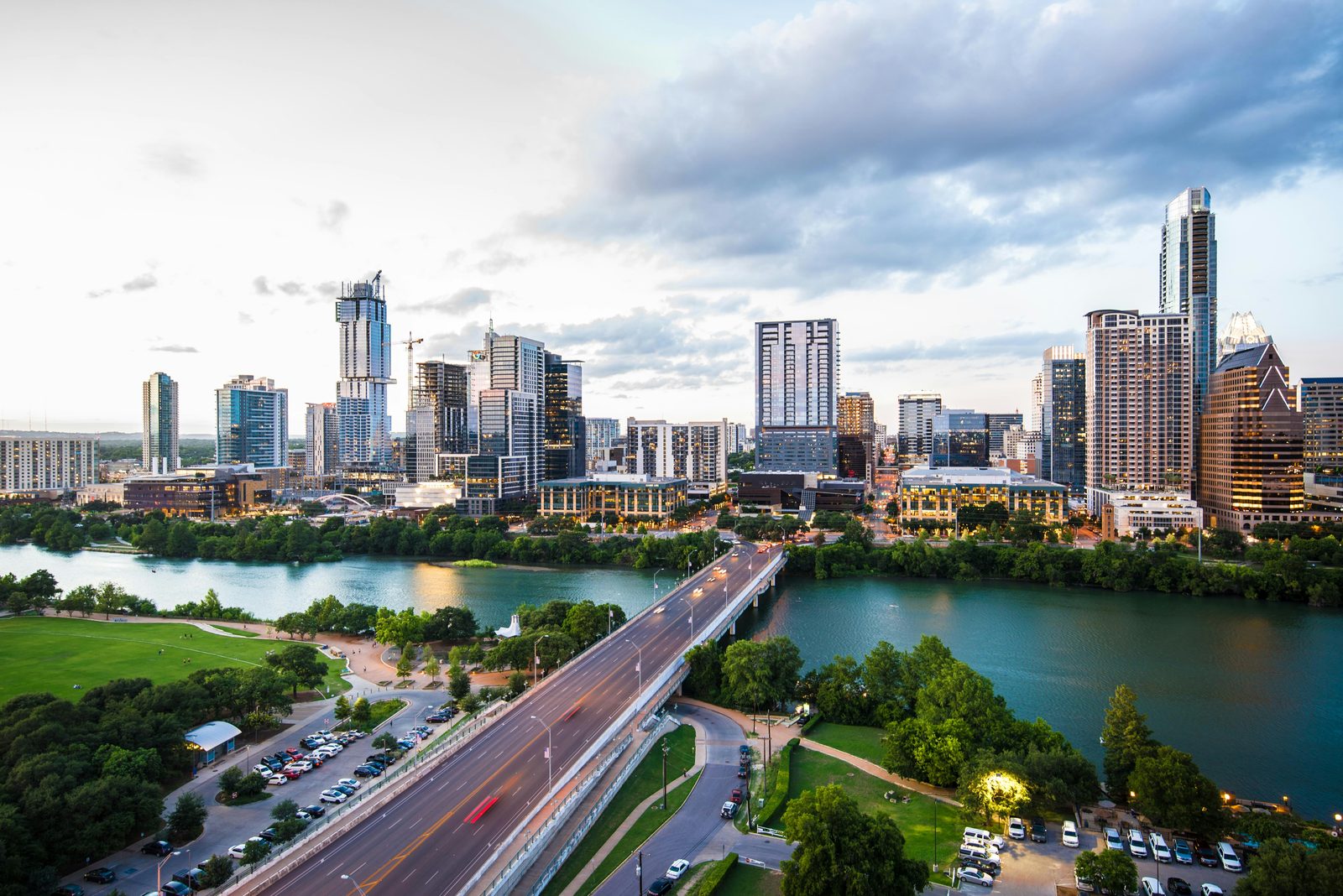 Austin's downtown skyline at dusk across Lady Bird Lake, with a construction crane and a half-built tower