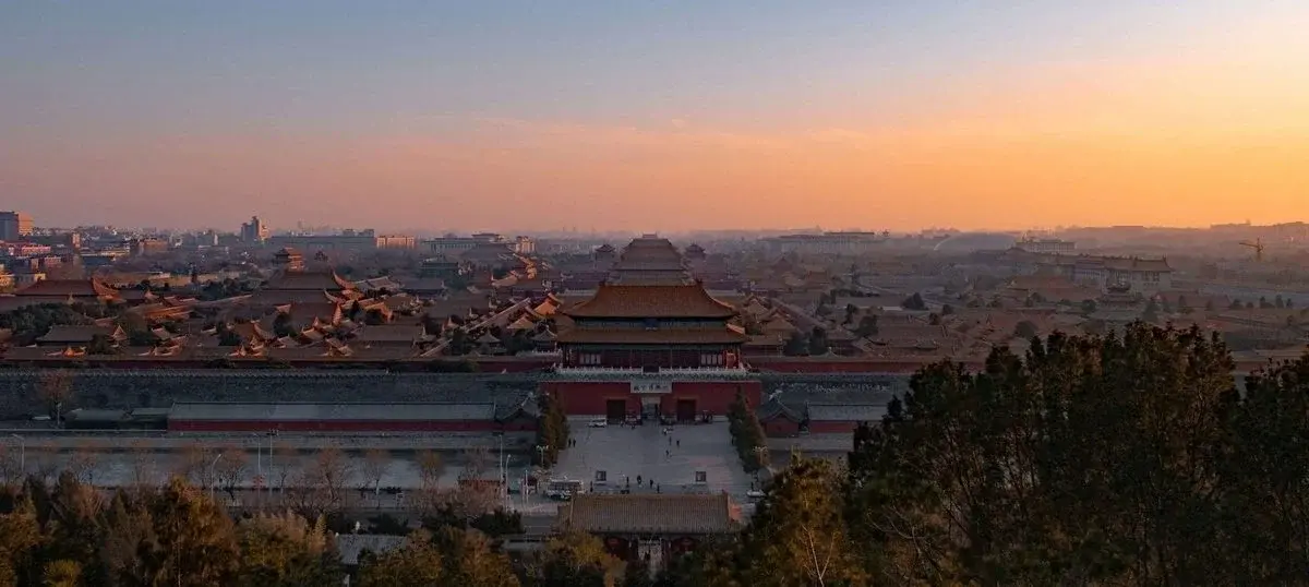 The Forbidden City's golden roofs stretching to the horizon at dusk, the modern city faint behind them