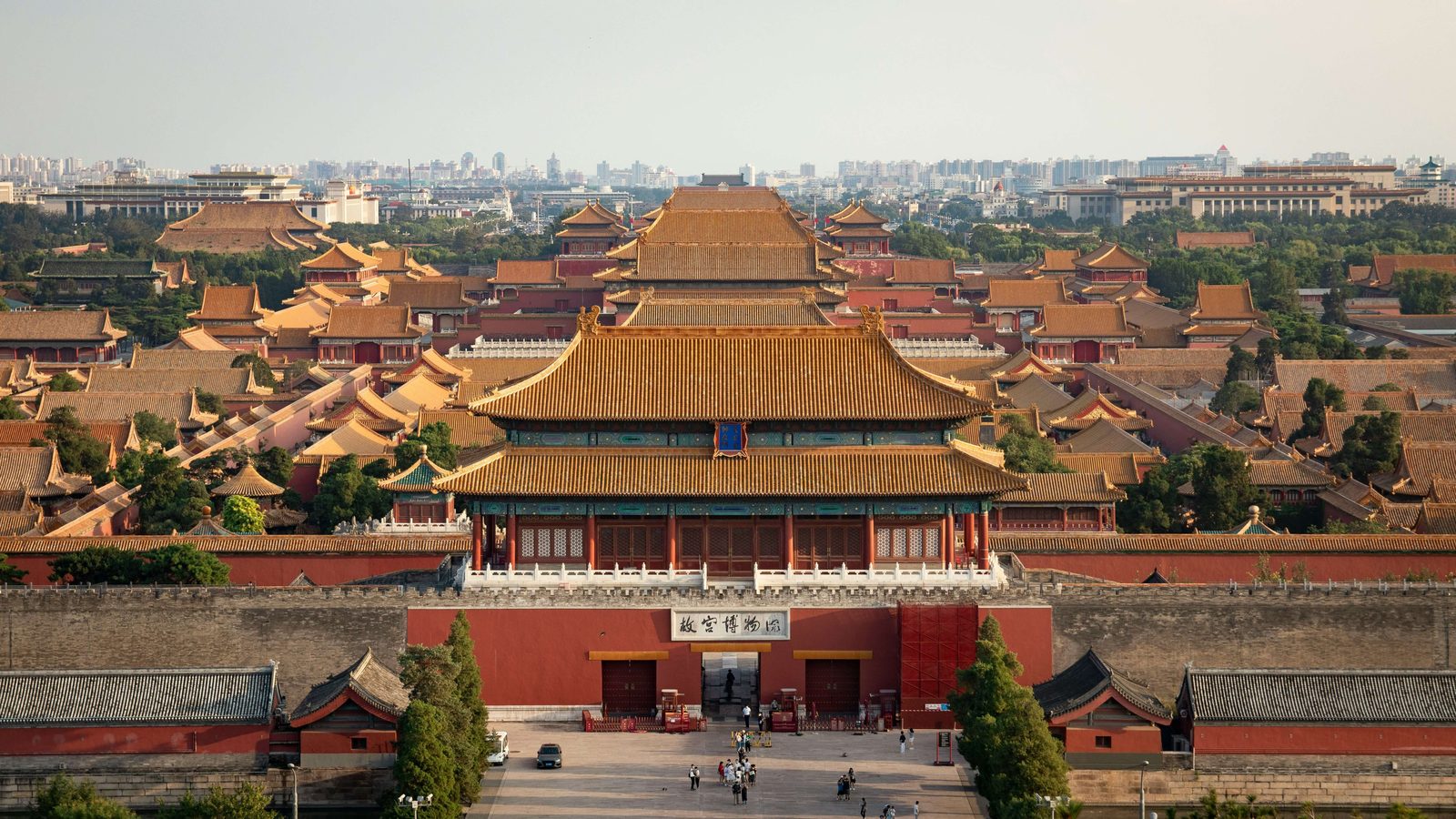The vermilion gate and grey brick wall of the Forbidden City, a single figure passing through the central arch