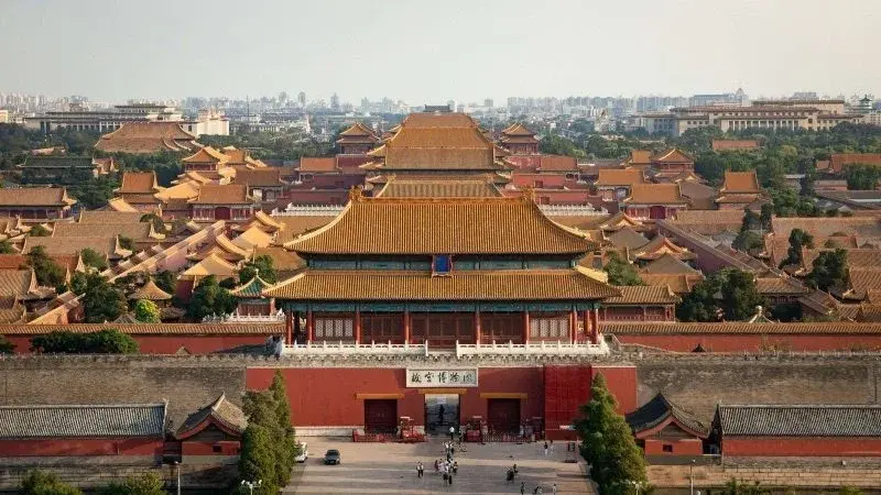 The vermilion gate and grey brick wall of the Forbidden City, a single figure passing through the central arch