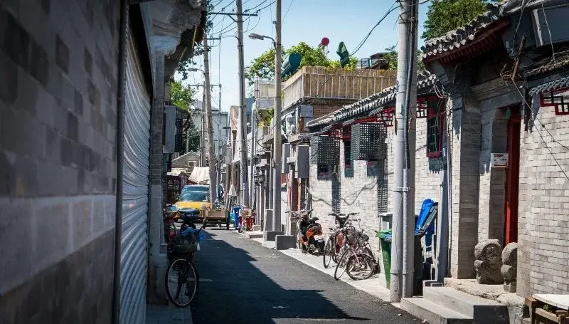 A narrow hutong alley in Beijing with bicycles parked along grey-brick courtyard walls
