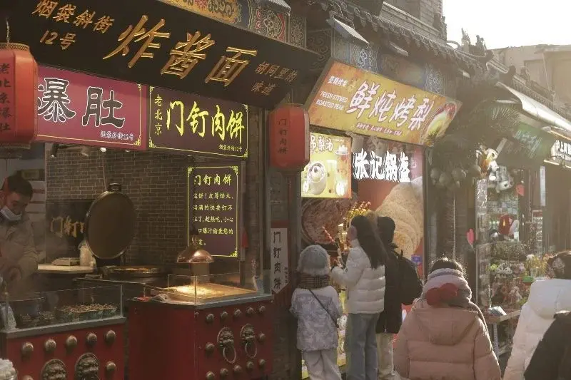 Hutong food stalls in Beijing with signage for baodu and zhajiangmian, customers browsing
