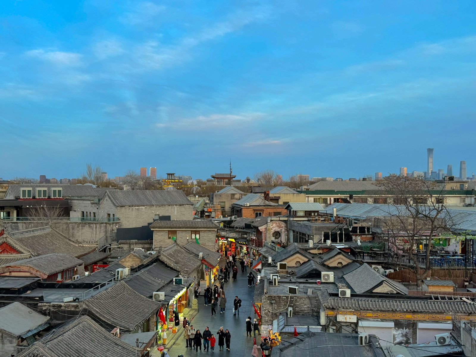 Grey brick hutong rooftops in the foreground with the distant CBD towers rising behind