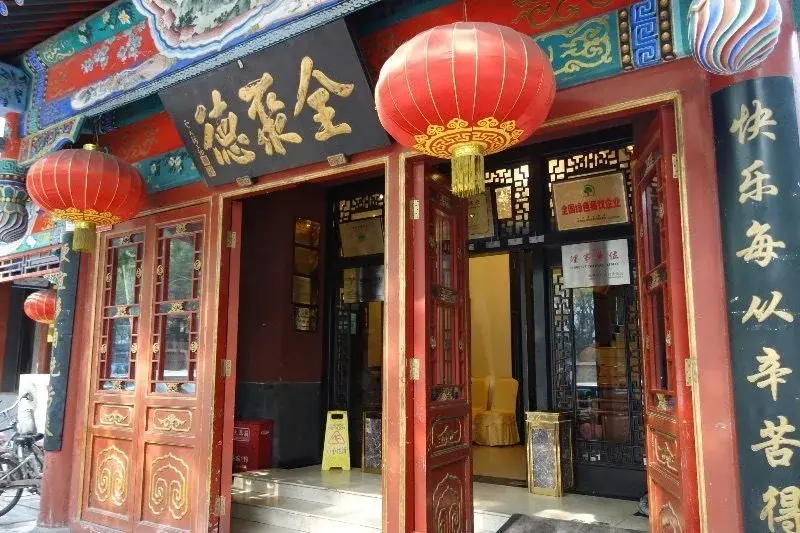 The red-lacquered storefront of a Quanjude roast duck restaurant, with red lanterns hanging over the entrance