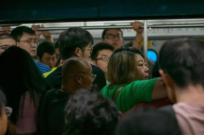 A packed Beijing subway car at rush hour, passengers pressed shoulder to shoulder holding the overhead rail