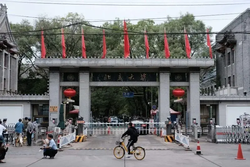 The gate of Peking University in Haidian, students and bicycles passing a guarded checkpoint