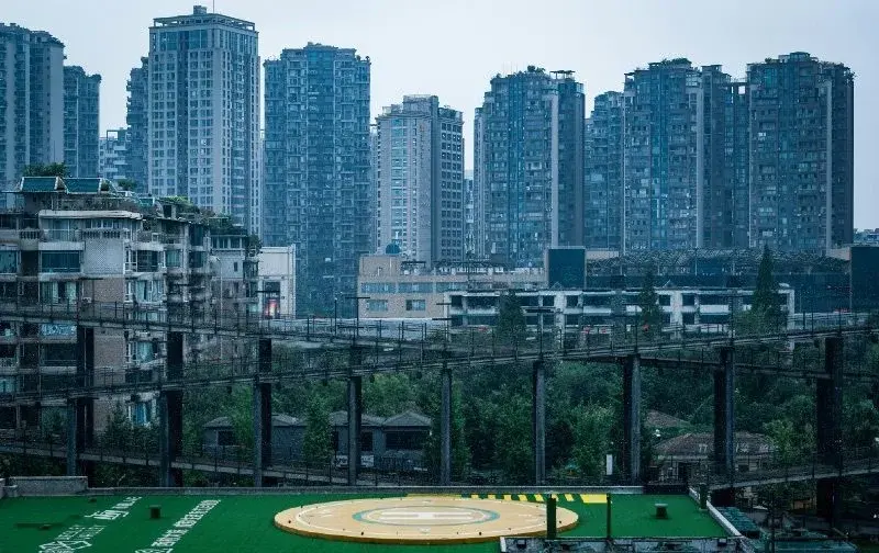 A row of modern high-rise apartment towers behind an elevated walkway and a helipad-marked rooftop in Chengdu