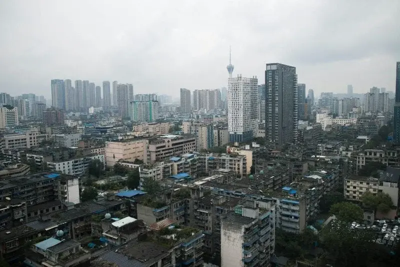 A dense skyline of older mid-rise apartment blocks in Chengdu under an overcast sky, with newer towers visible behind