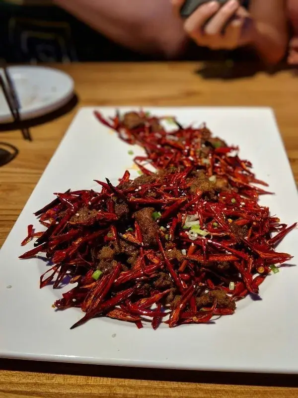 A dish of dry-fried chili peppers and beef, the chilies far outnumbering the meat, served on a white plate