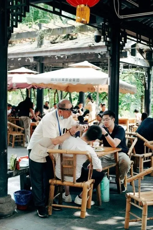 An ear-cleaning master with a headlamp working on a customer seated in a bamboo chair at a Chengdu teahouse
