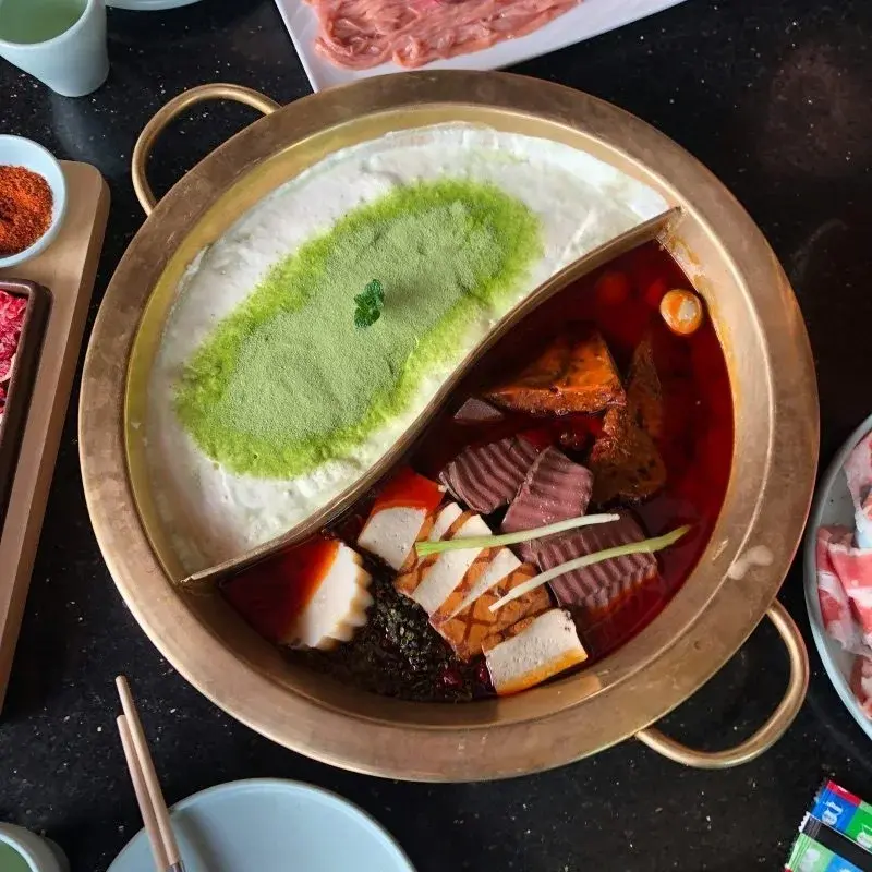 A divided Sichuan hotpot — one side milky broth, one side deep red chili oil filled with tofu and blood cake