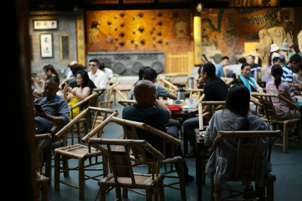 A traditional Chengdu teahouse with bamboo chairs and lidded tea bowls, filled with people