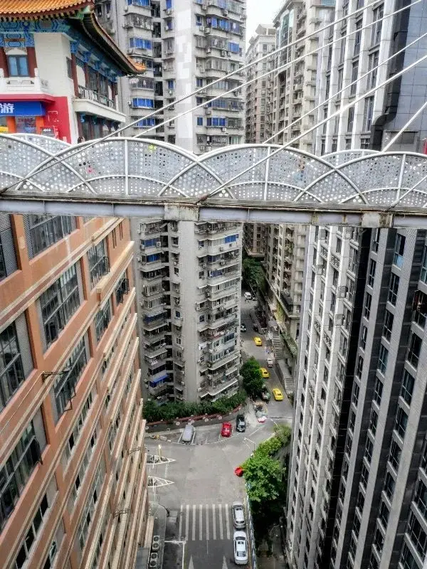 Looking down from the Kuixing Lou skybridge in Chongqing at a residential tower built down a hillside, with a red-and-gold pavilion rooftop visible at the same level as the bridge deck