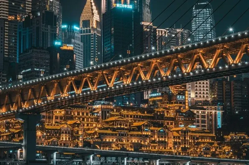 Hongyadong stilt-house buildings lit up at night in Chongqing, seen from a bridge over the river