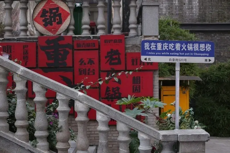 A wall of red hand-painted restaurant signs in Chongqing, including a blue street sign reading 'I miss you while eating hot pot in Chongqing'