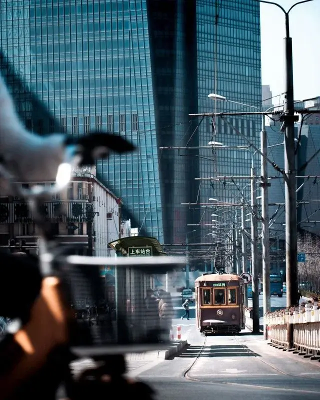 An old Route 201 tram car running on a Dalian street, glass office towers rising behind it