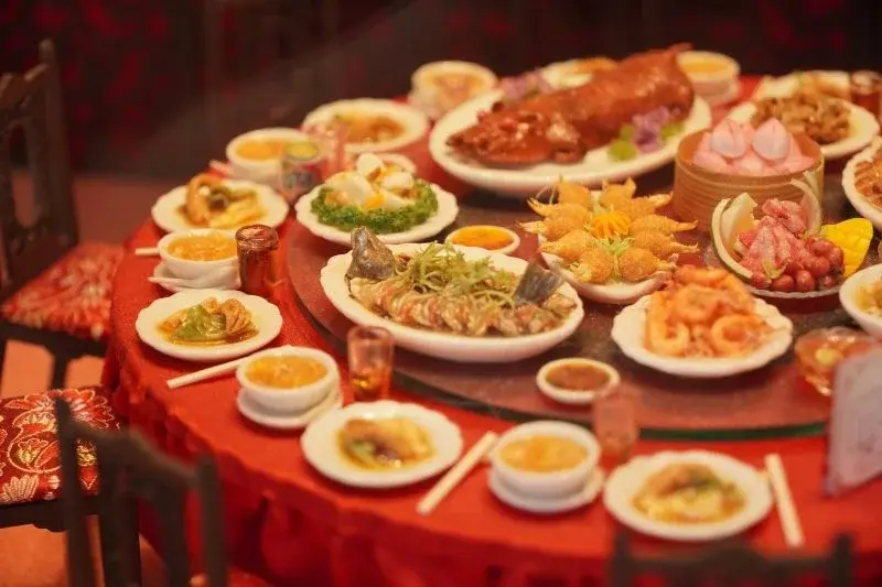 A round Cantonese banquet table crowded with dishes, centered on a whole roast suckling pig, with steamed seafood, dim sum, and dessert plates arranged around it