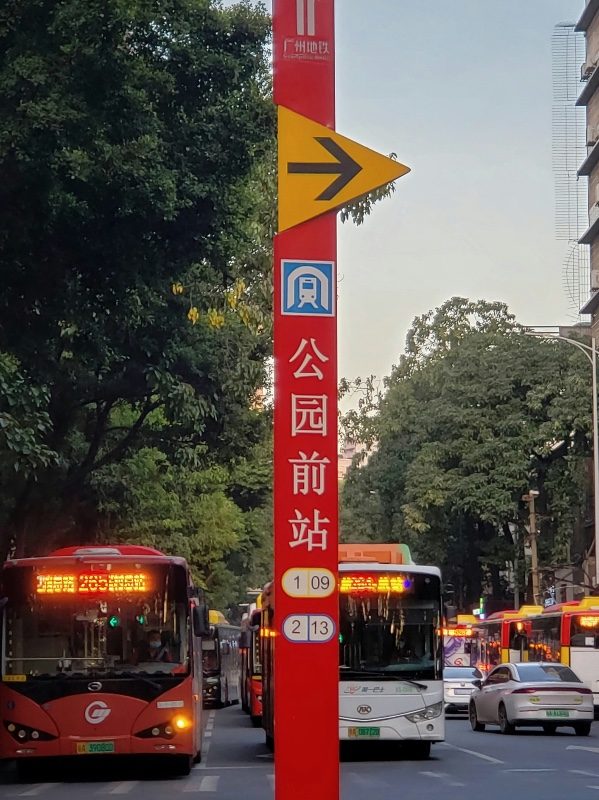 A red Guangzhou Metro street sign on Beijing Road showing a directional arrow, the metro logo, and the station name Gongyuanqian, with numbered bus routes listed below