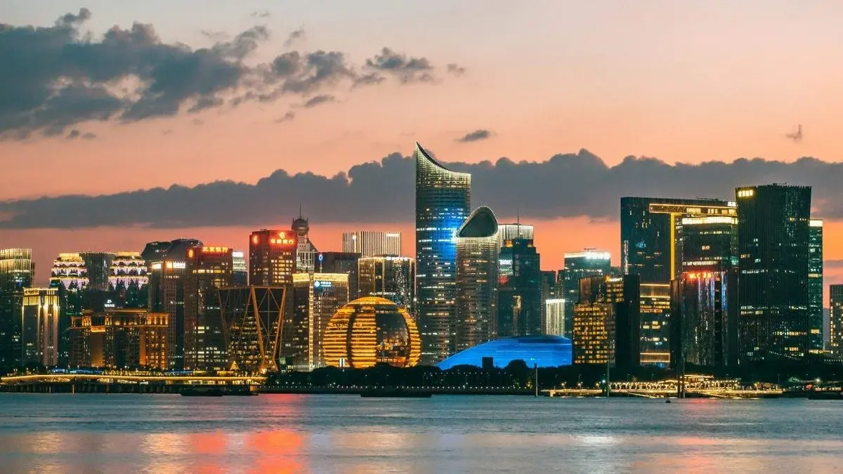 Hangzhou's Qianjiang New Town skyline at sunset, the golden ring-shaped tower lit up beside the river, dramatic clouds overhead