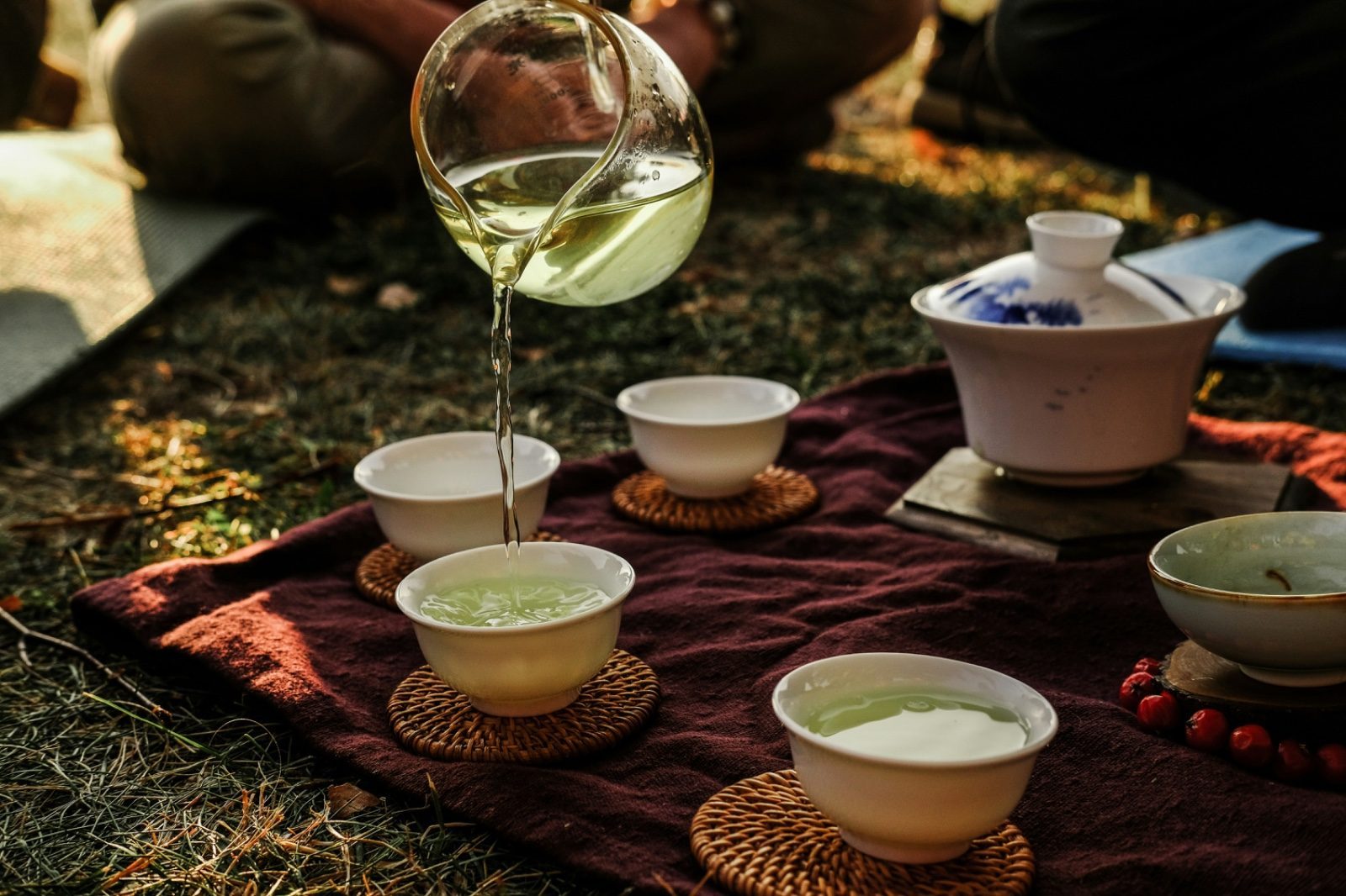 Gongfu-style tea being poured from a glass fairness cup into small cups arranged on a mat near Hangzhou