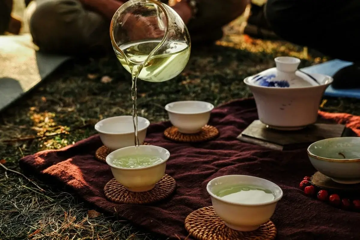 Gongfu-style tea being poured from a glass fairness cup into small cups arranged on a mat near Hangzhou