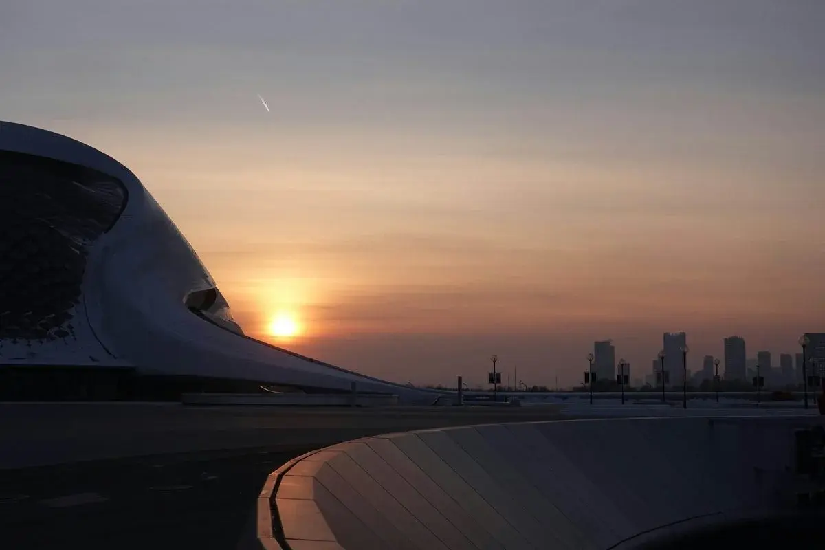 Harbin Opera House, a curved white modern building, silhouetted at sunset with the city skyline behind