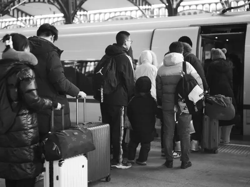 A black-and-white photo of a family boarding a train with rolling suitcases and bags at a Harbin station platform