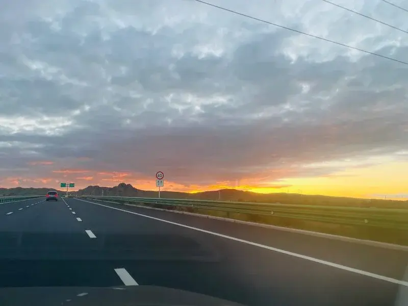 A wide highway at sunset with orange and pink sky near Hohhot, the road stretching toward the horizon