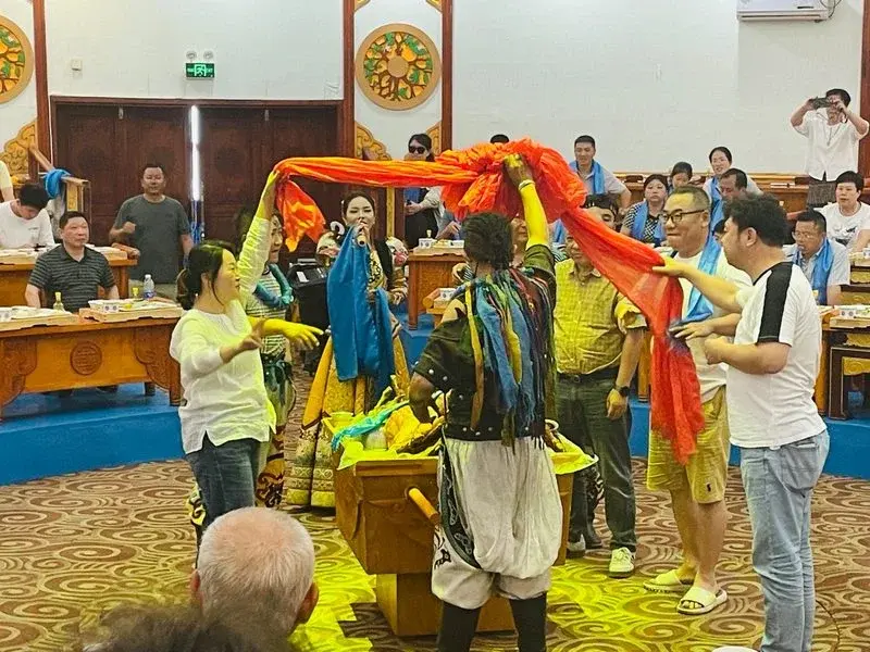 Performers in traditional dress holding an orange ceremonial scarf over a guest at a zhamayan feast hall in Hohhot