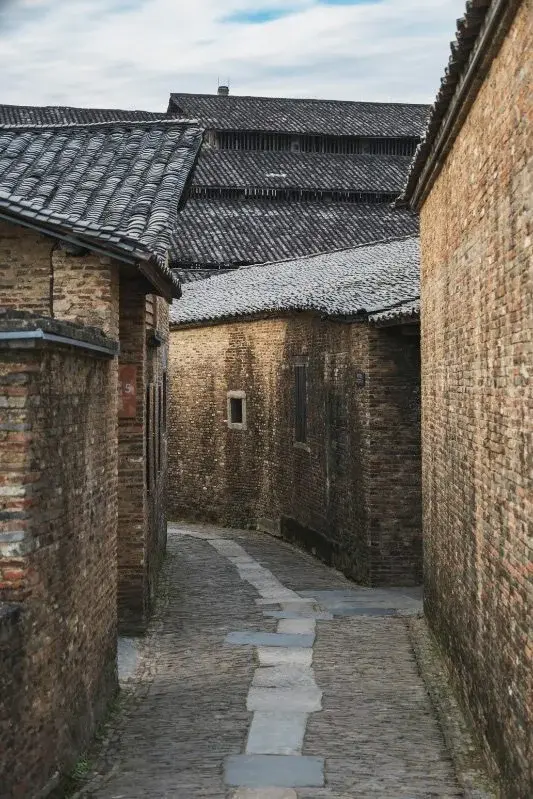 A narrow stone alley between old brick buildings in Jingdezhen, the upper walls built from stacked cylindrical kiln saggars instead of ordinary brick