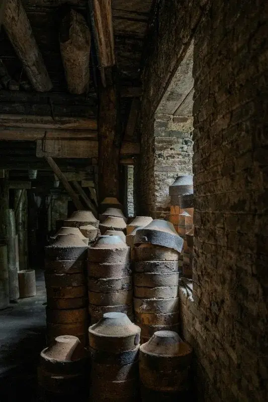 Stacked cylindrical clay saggars inside a dim, wood-beamed kiln workshop