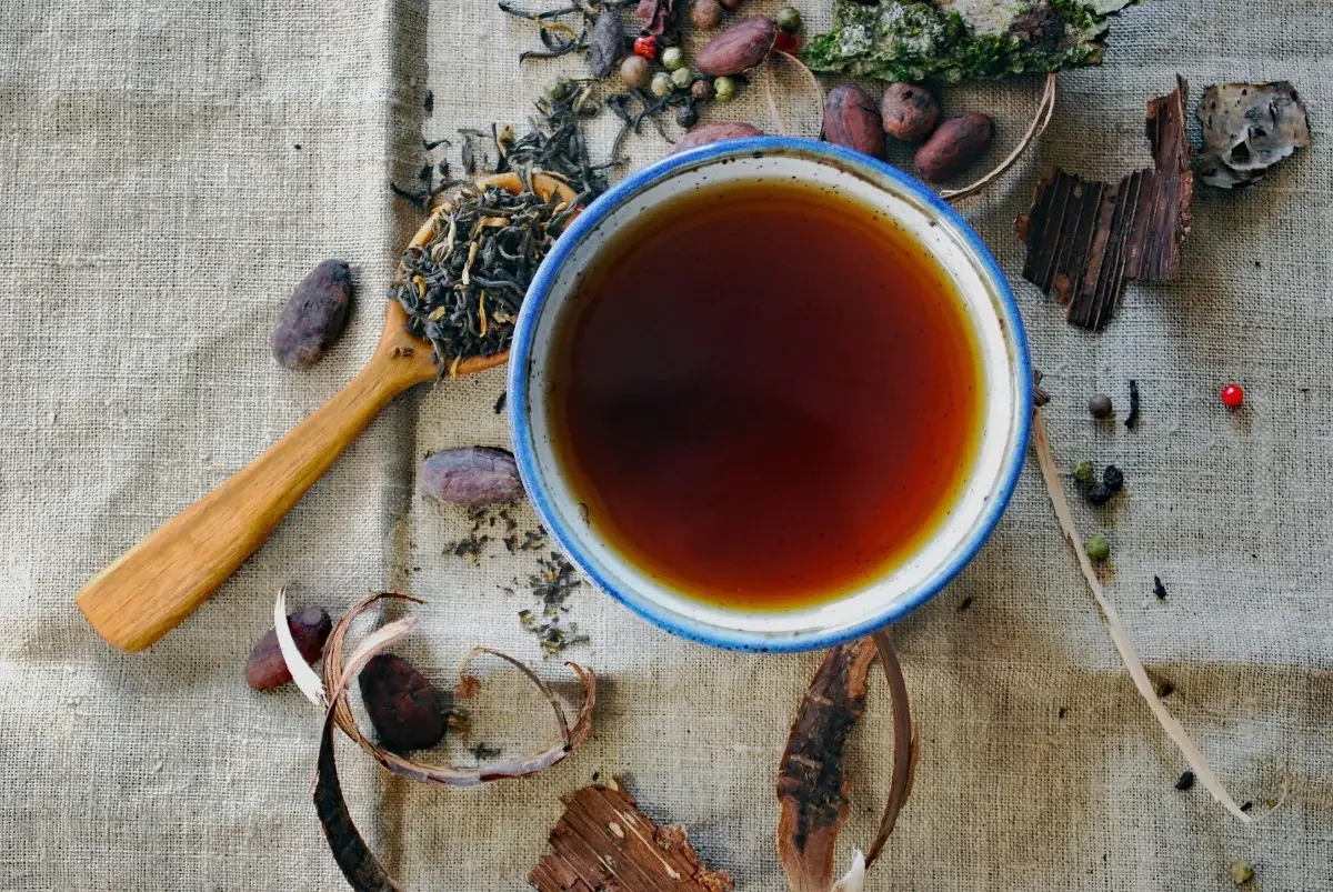 A cup of dark-brewed Yunnan black tea surrounded by loose tea leaves and dried spices