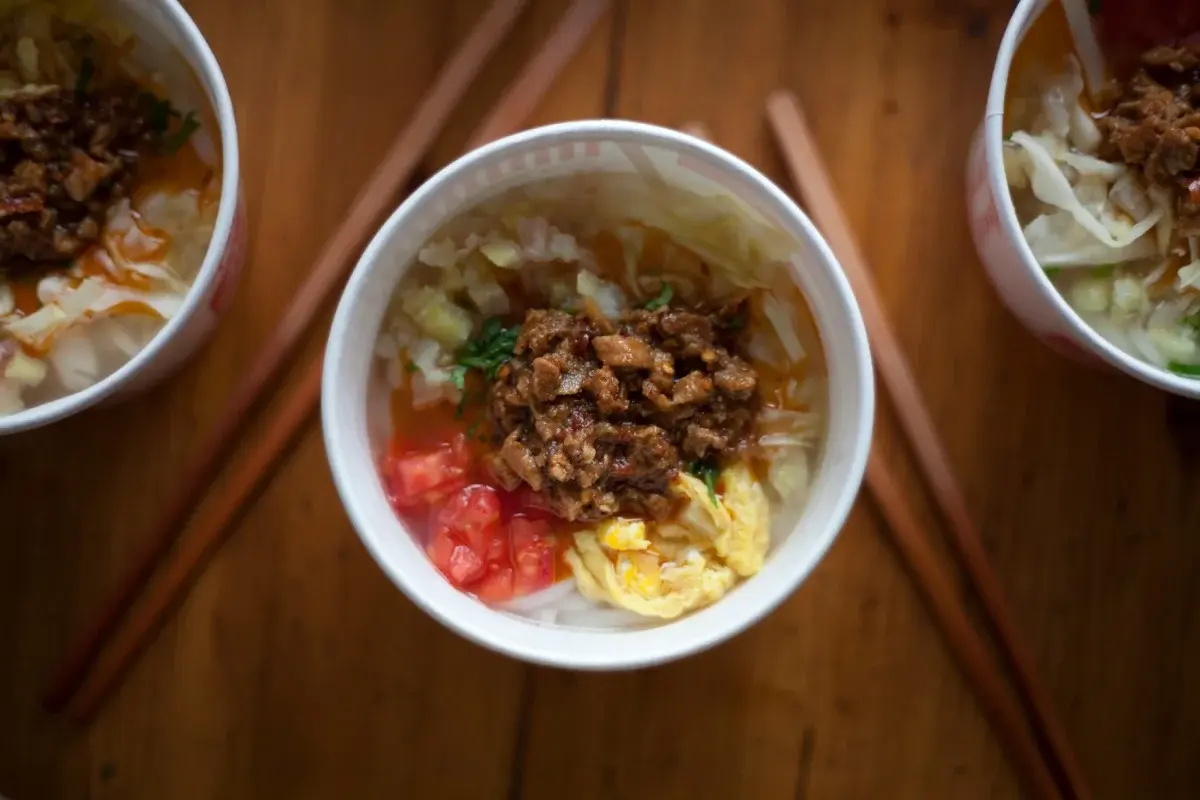 A bowl of Kunming rice noodle soup topped with scallions and minced pork, with fried dough sticks alongside