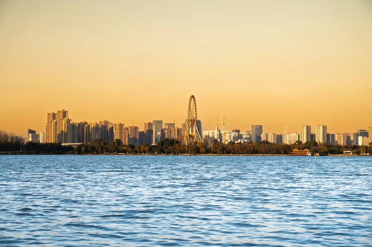 Kunming's skyline seen from a forested ridge, high-rises spreading toward Dianchi Lake
