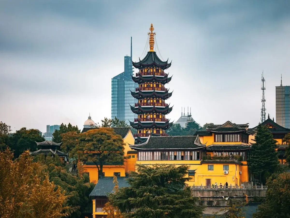 The multi-tiered pagoda of Jiming Temple rising above its yellow walls, with a modern skyscraper visible behind it in Nanjing