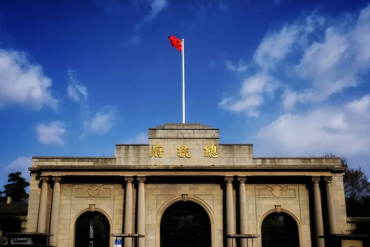 The gate of the Presidential Palace in Nanjing, gold Chinese characters reading 'Presidential Palace' above three arched doorways, a red flag flying above