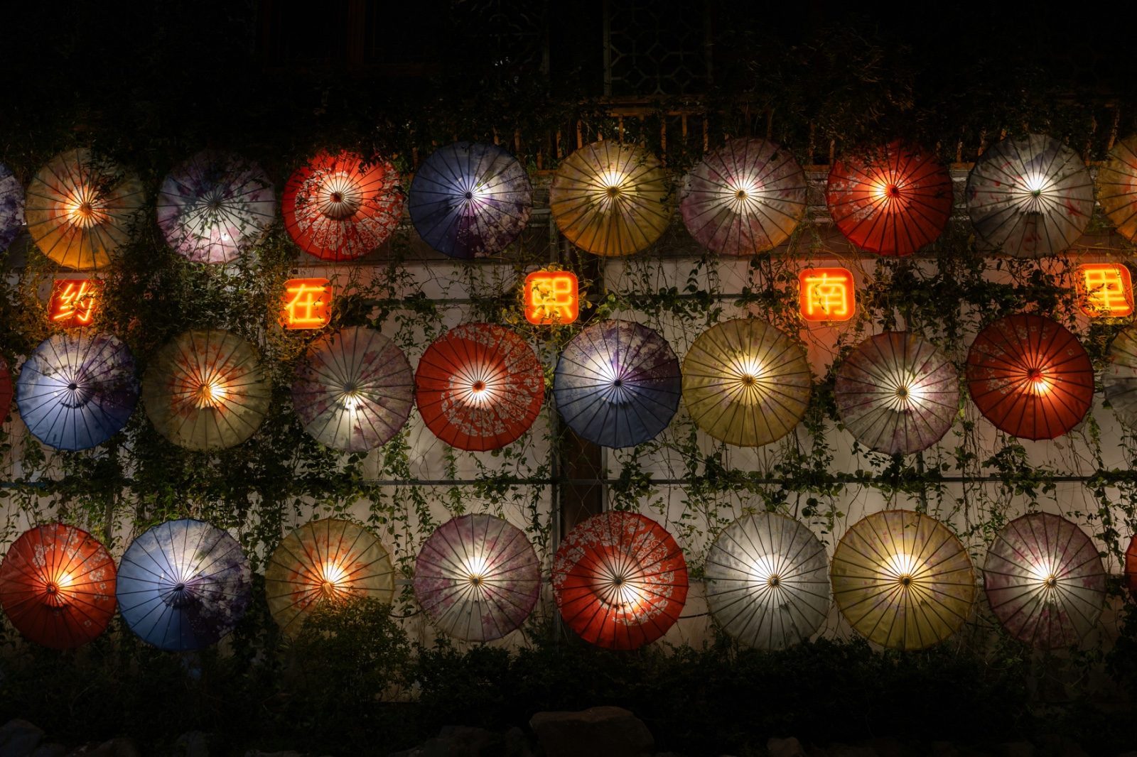Rows of illuminated paper umbrellas hung as lanterns at night in Nanjing's old town, with a red neon sign reading 'Nanjing' among them
