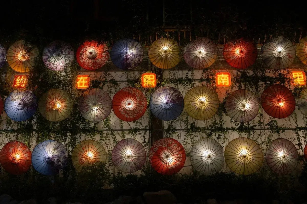 Rows of illuminated paper umbrellas hung as lanterns at night in Nanjing's old town, with a red neon sign reading 'Nanjing' among them