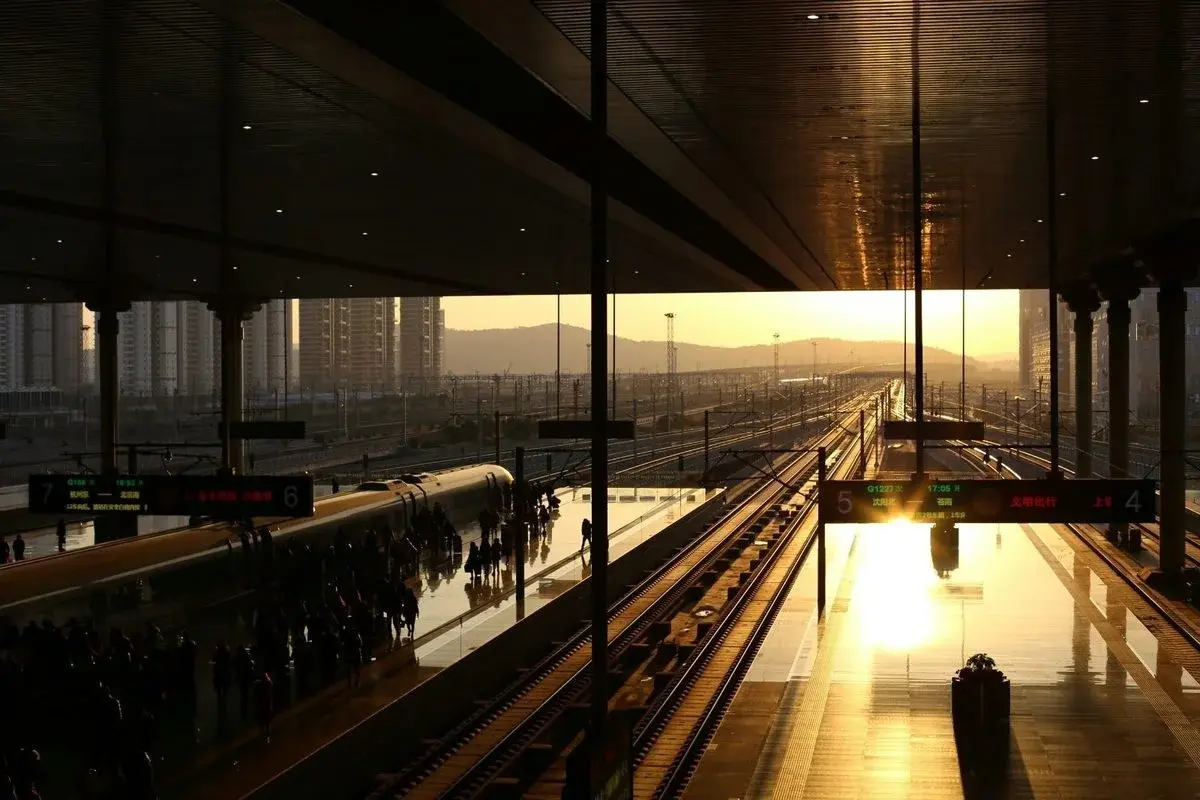 A high-speed rail platform at sunset, a train pulling in as passengers wait, departure boards showing routes to Hangzhou East, Beijing South and Shenyang North