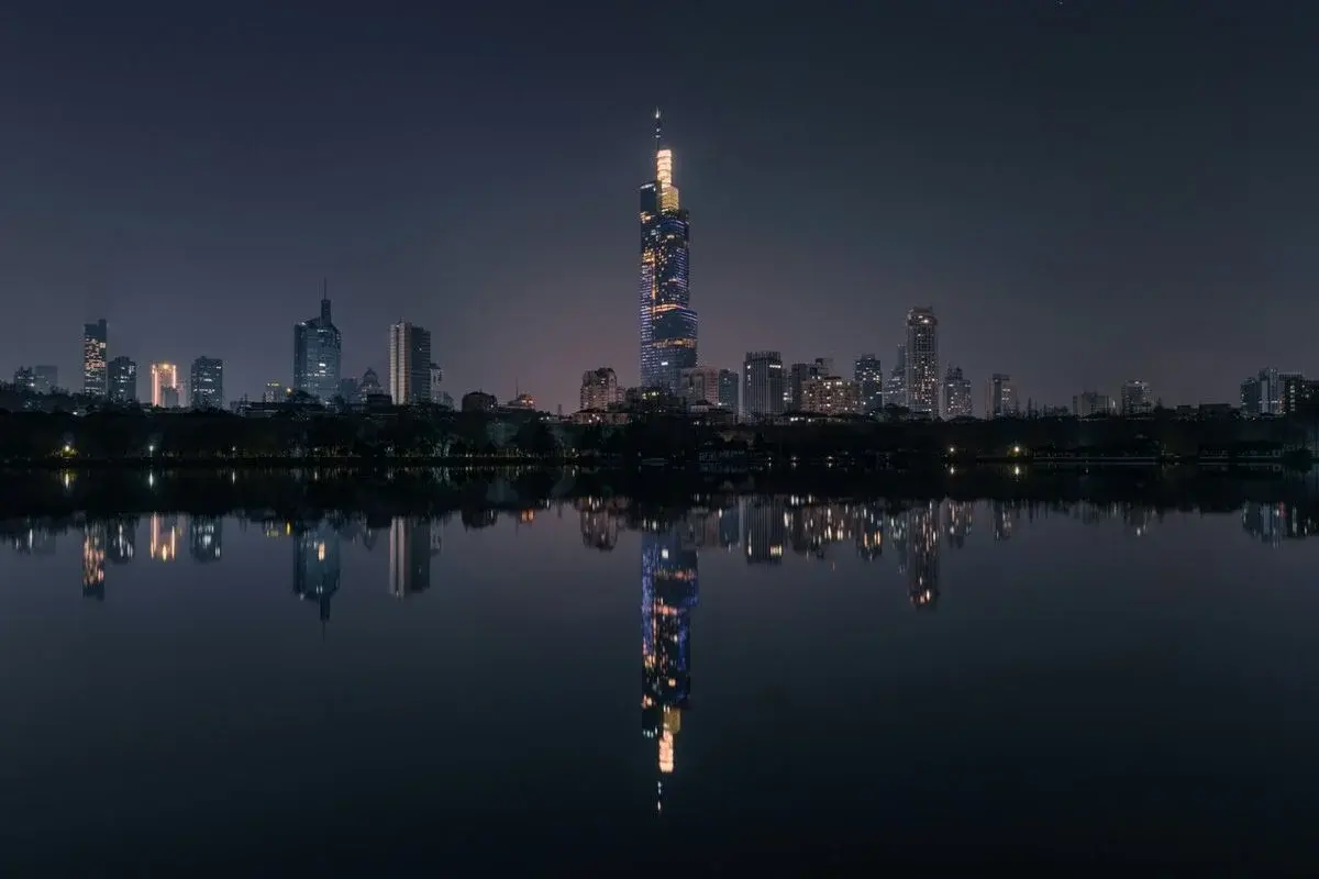 The Zifeng Tower lit up at night, reflected in a still lake alongside the rest of Nanjing's financial-district skyline
