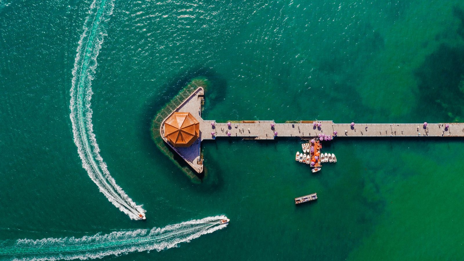 Aerial view of Zhan Qiao pier extending into turquoise water, with speedboats leaving white wakes on either side