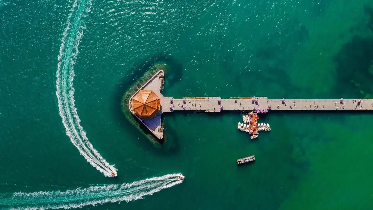 Aerial view of Zhan Qiao pier extending into turquoise water, with speedboats leaving white wakes on either side