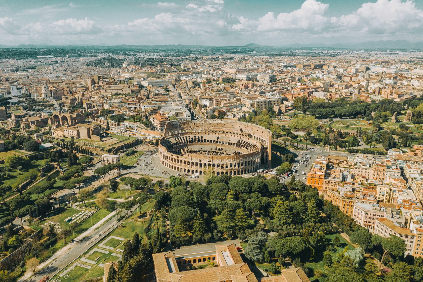 Aerial view of the Colosseum and Roman Forum embedded in the modern city, ringed by streets and traffic