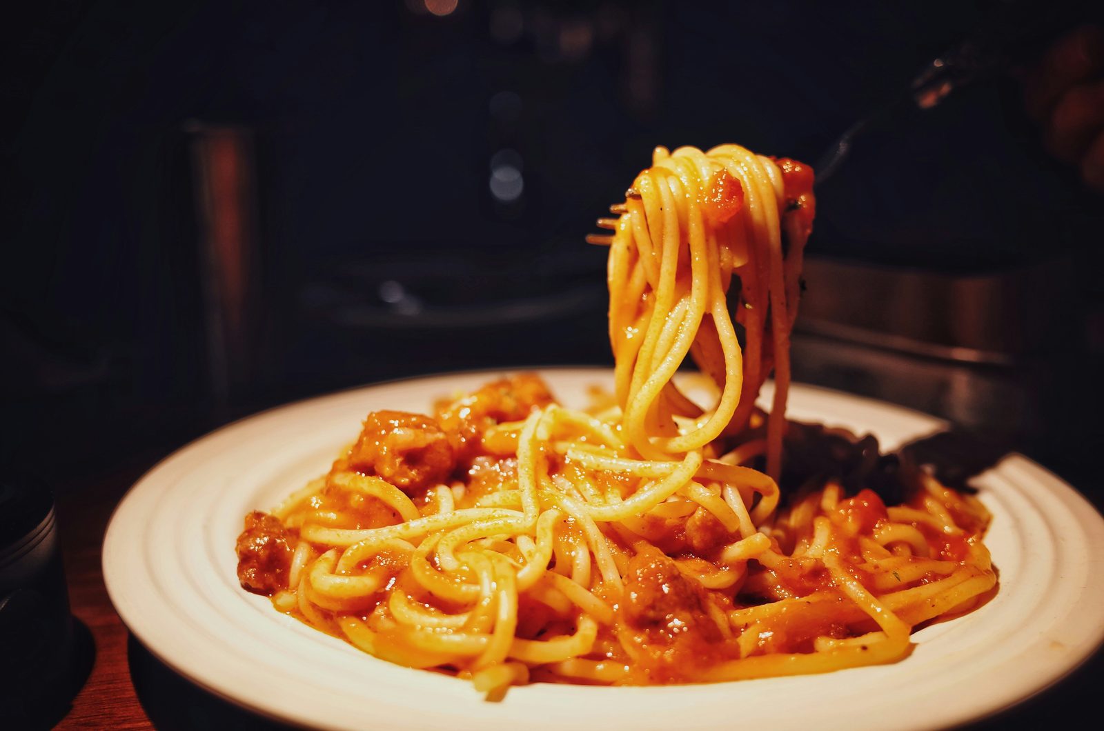 A fork lifting a twirl of spaghetti in tomato sauce from a plate