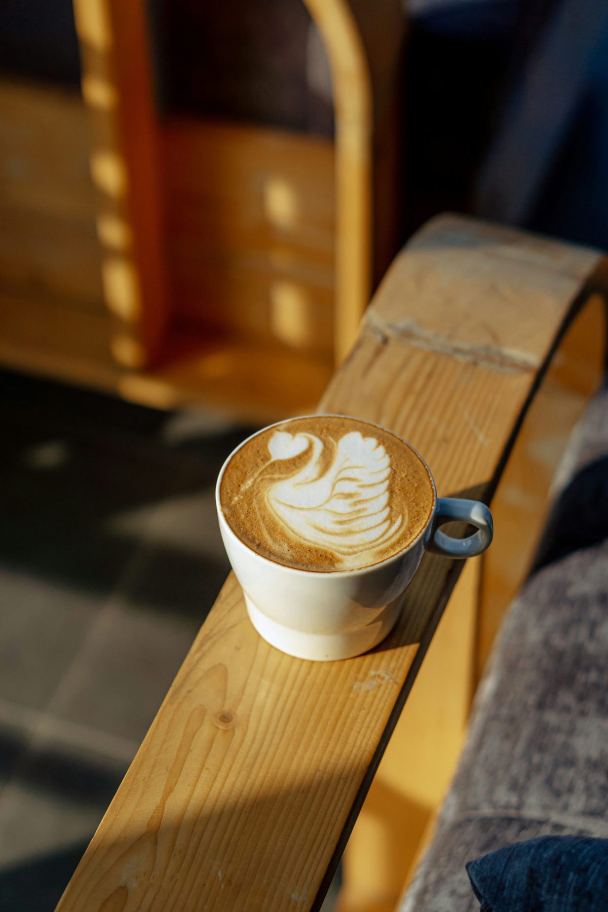 A latte with swan art resting on a sunlit wooden café bench