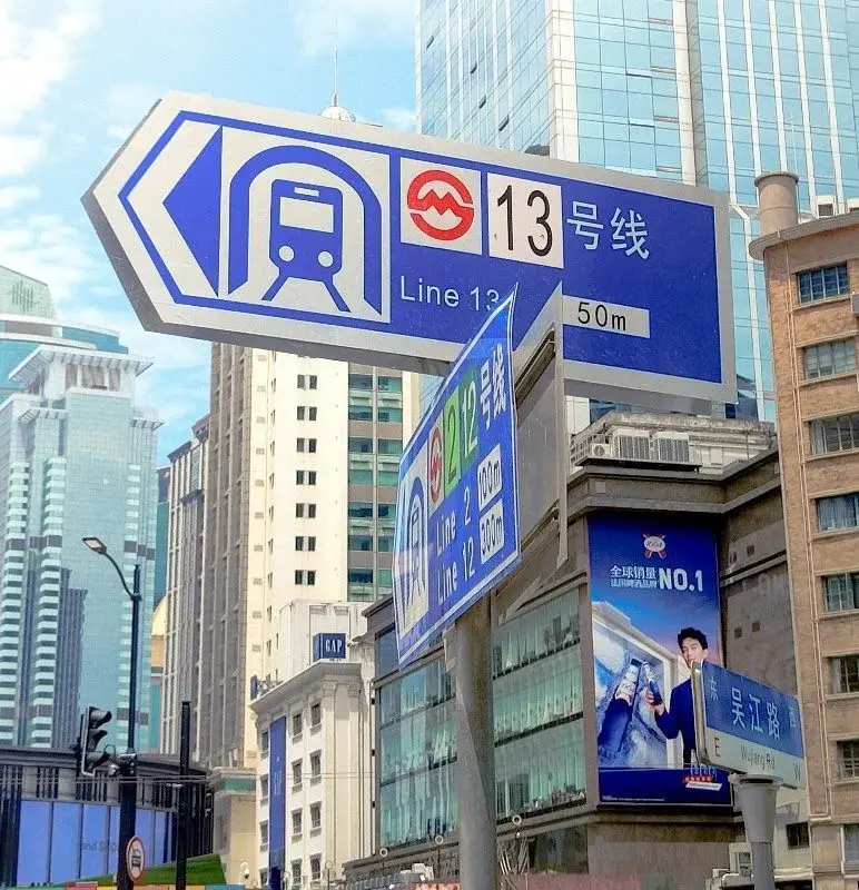 Blue street signage in Shanghai pointing toward Metro Line 13, with Line 2 and Line 12 signs stacked below, each showing the network's red-swirl logo