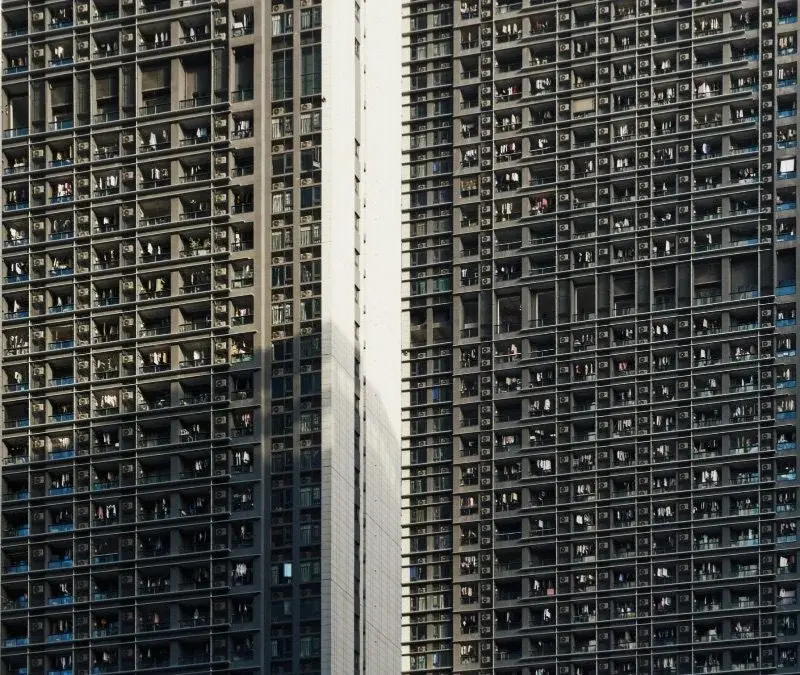 A close-up view of two dense high-rise apartment towers in Shenzhen, dozens of balconies stacked floor after floor, laundry and air conditioning units visible on nearly every one
