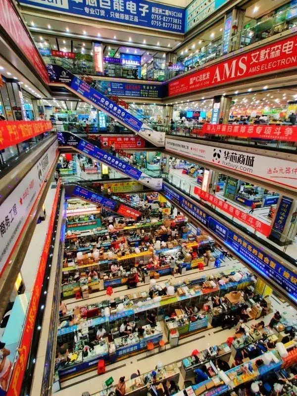 A multi-story view down into Huaqiangbei's electronics market in Shenzhen, escalators crossing between floors of component stalls and signage