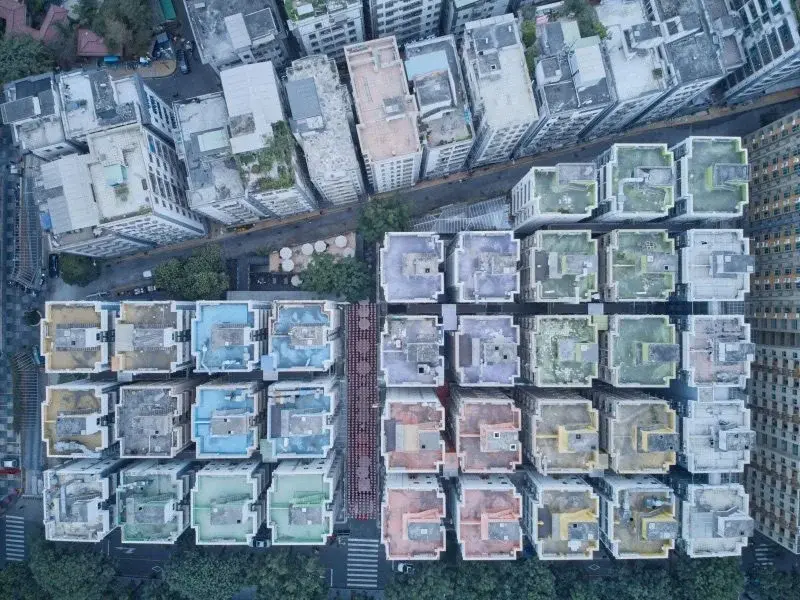 Aerial view of a dense Shenzhen urban village (chengzhongcun): tightly packed low-rise blocks with colorful rooftops and a central pedestrian lane