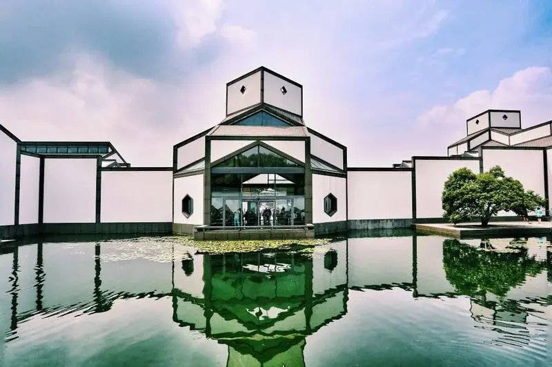 The Suzhou Museum's geometric white-and-grey ink-wash-inspired building, reflected in a lotus pond